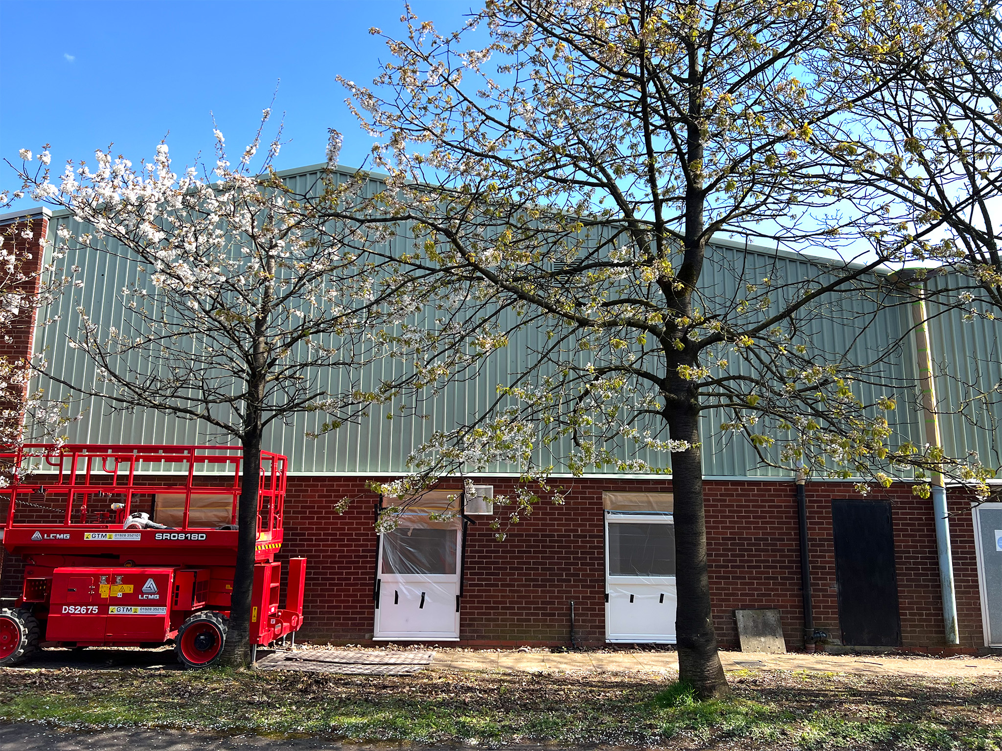 Red scissor lift gable cladding cherry blossom trees