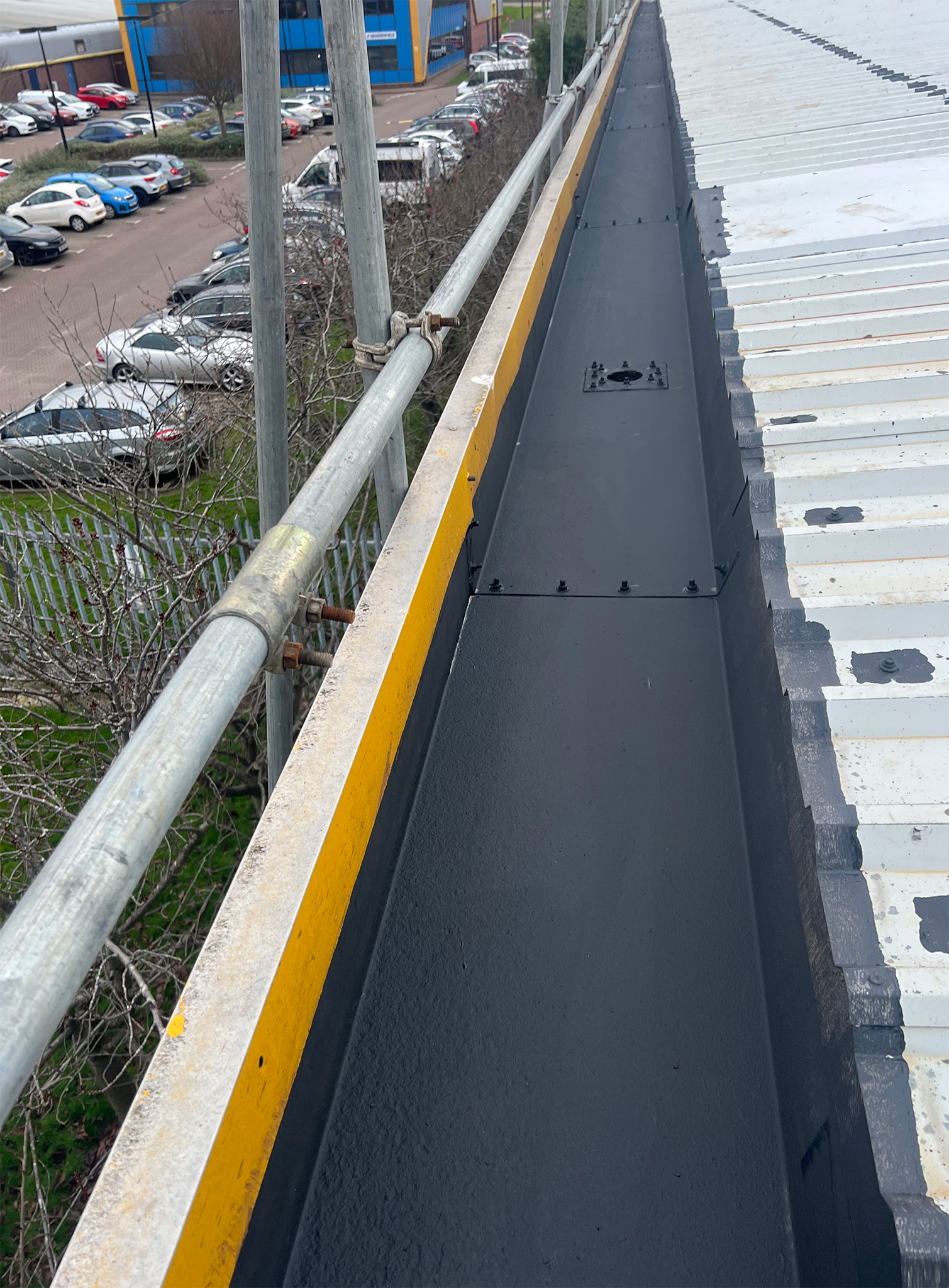 External steel box gutter fully coated with Everbuild Black Jack 902 bituminous primer, showing uniform coverage across the gutter channel, internal faces and upper flanges as part of the Gateshead PVF2 roof refurbishment