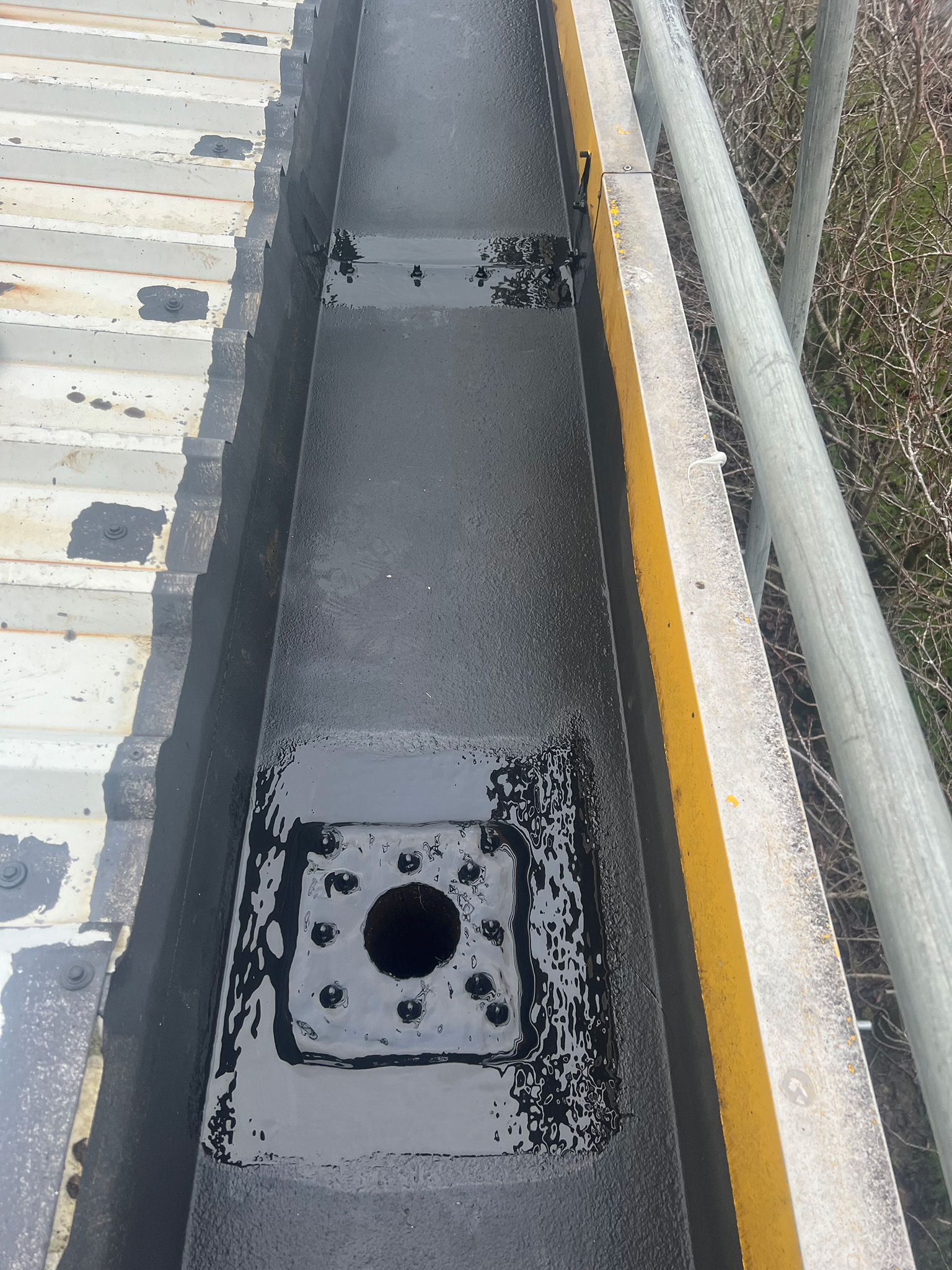 Steel gutter downspout outlets and gutter joint details treated with Everbuild Black Jack 902 primer and DriSilane ReTrim finishing coat, showing the completed two-coat protective system around the outlet socket and surrounding gutter base
