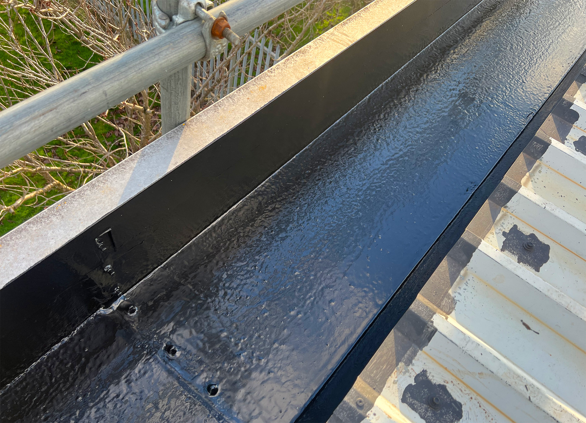Completed DriSilane ReTrim gutter protection coating on an external steel box gutter, showing the dry, uniform black finish across the full length of the gutter channel, joint details and downspout area