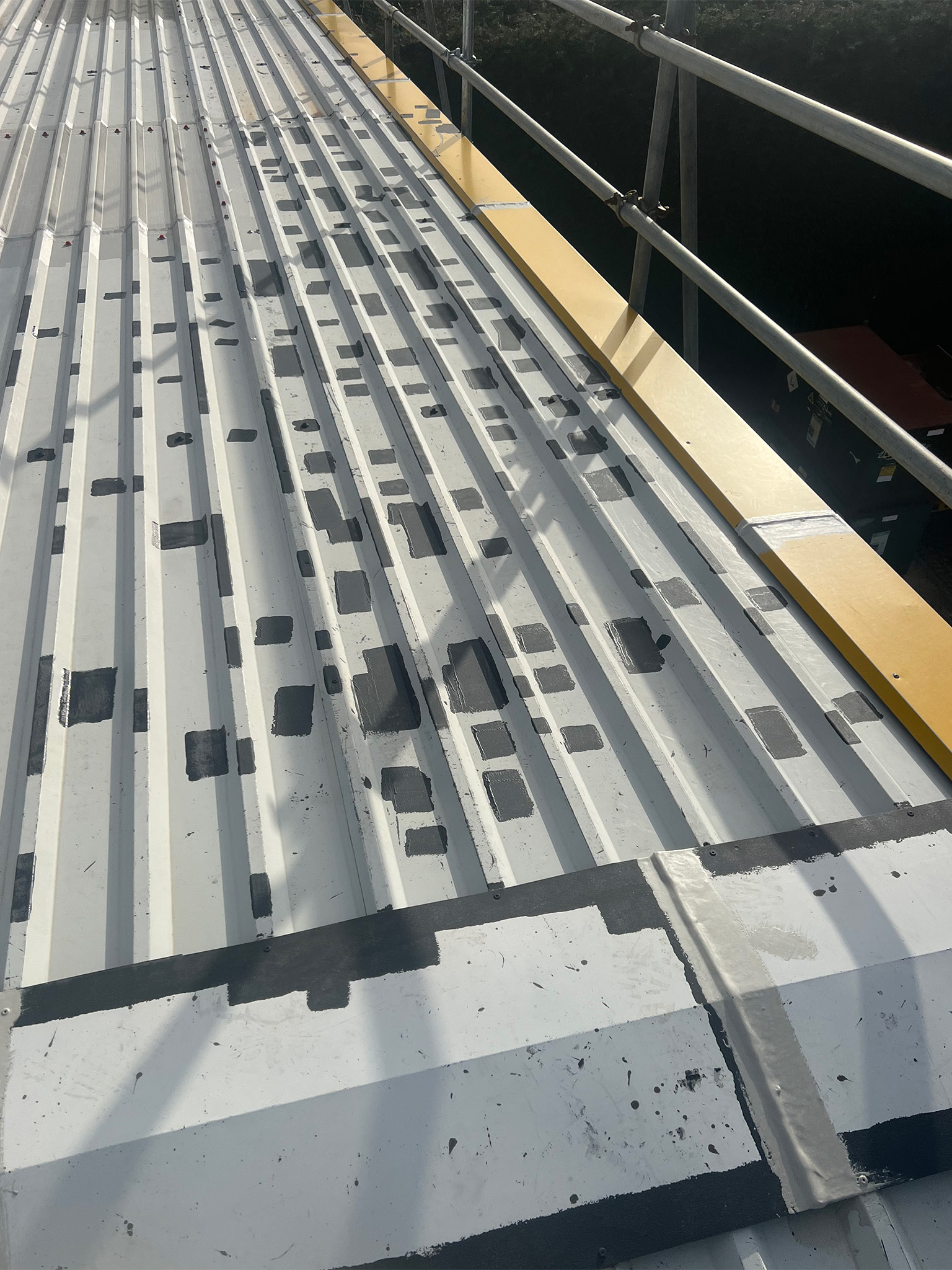 Numerous rust spots and areas of pitting corrosion on a profiled steel commercial roof, each individually treated by grinding and primed with Everbuild Black Jack 902 prior to overcoating