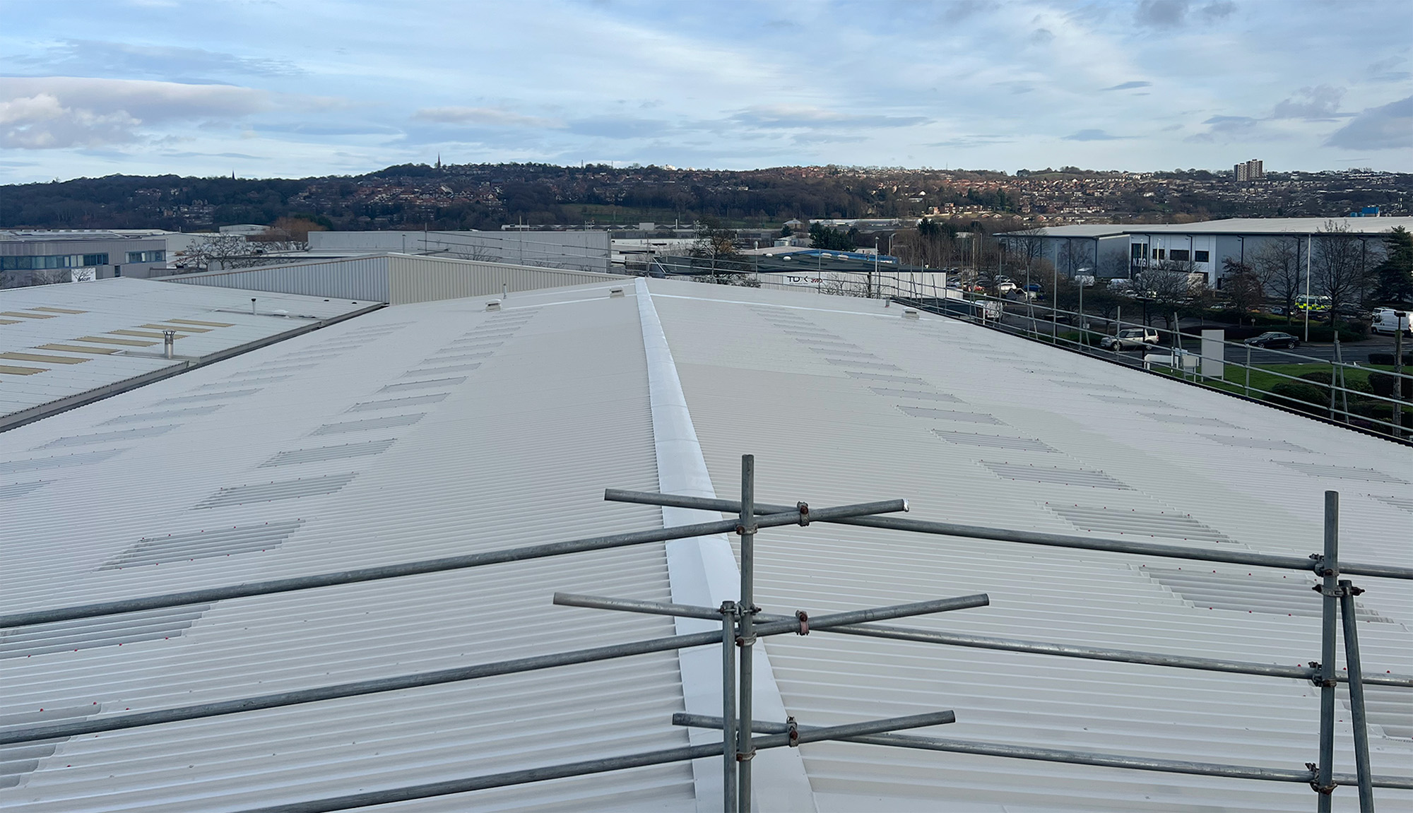 Panoramic view of a completed PVF2 roof refurbishment at a large office building in Gateshead, showing freshly spray-applied DriSilane roof coat across the full extent of the profiled steel sheeting