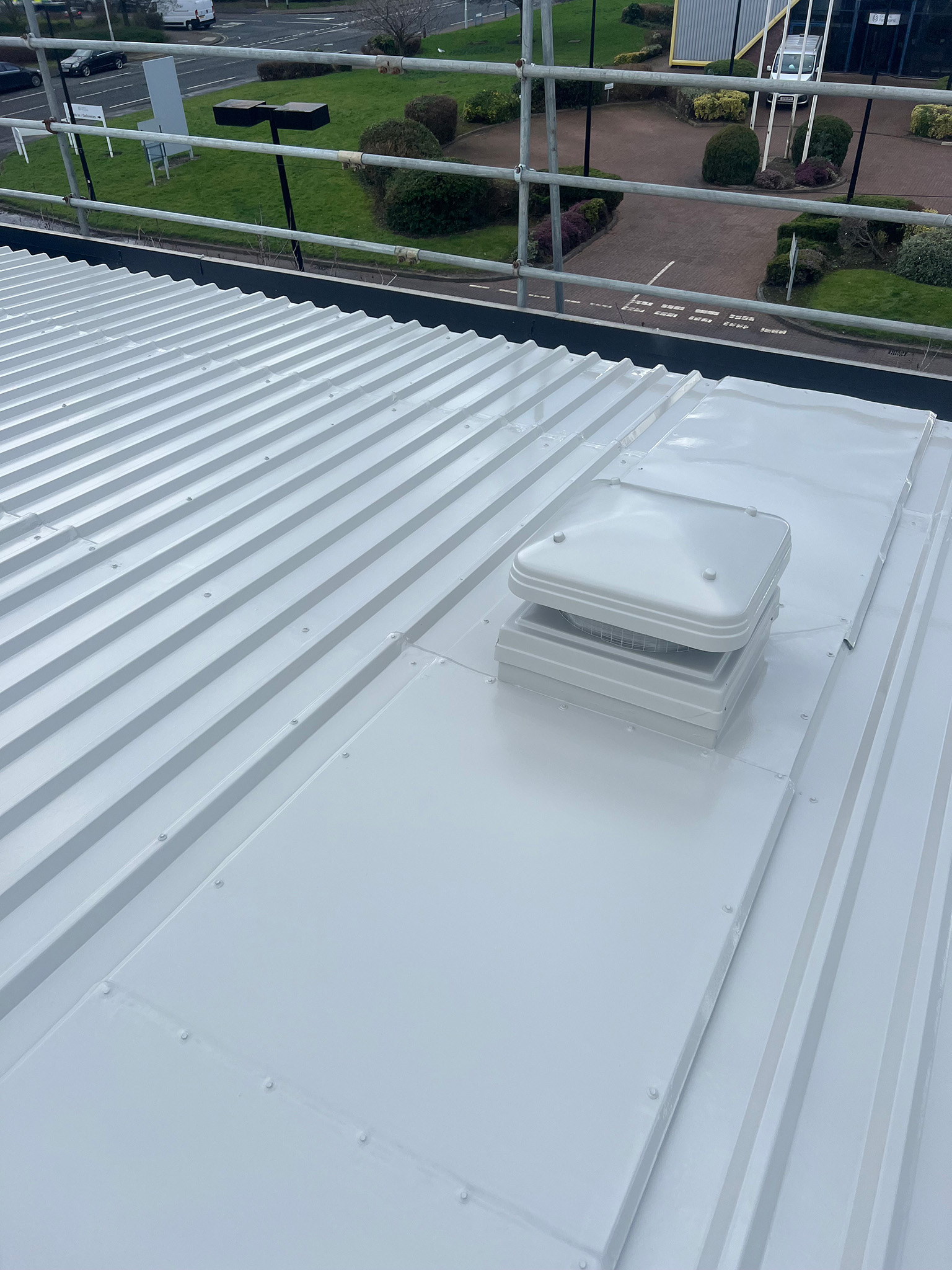 Roof-mounted ventilation cowl and surrounding steel sheeting freshly coated with DriSilane roof coating system, showing full coverage of the cowl base flashing, adjacent profiled steel sheets and fixings
