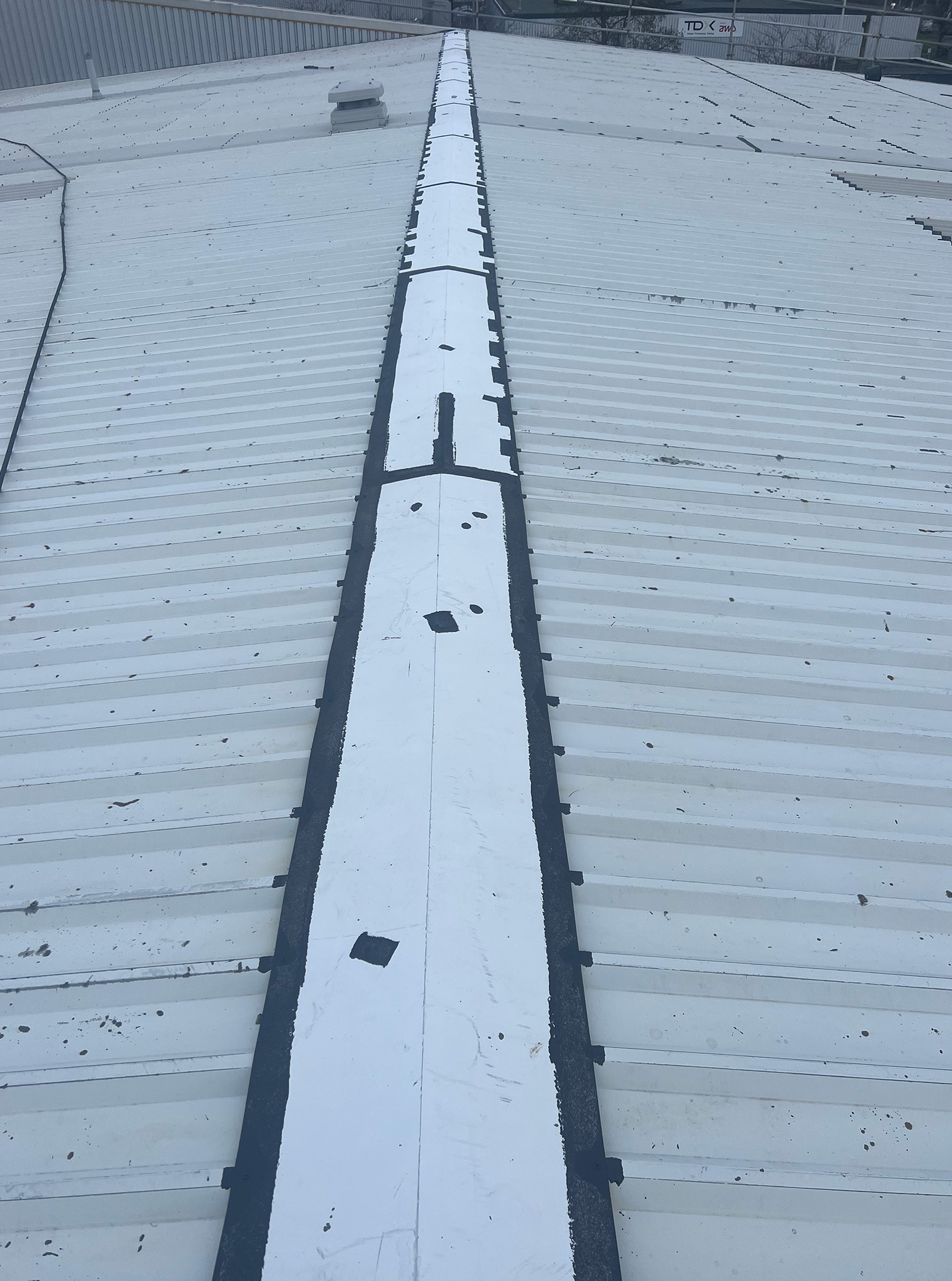 Steel roof ridge cap with exposed cut edges, lap joints and rust spots treated and spot-primed with Everbuild Black Jack 902 primer as part of the PVF2 roof refurbishment surface preparation works