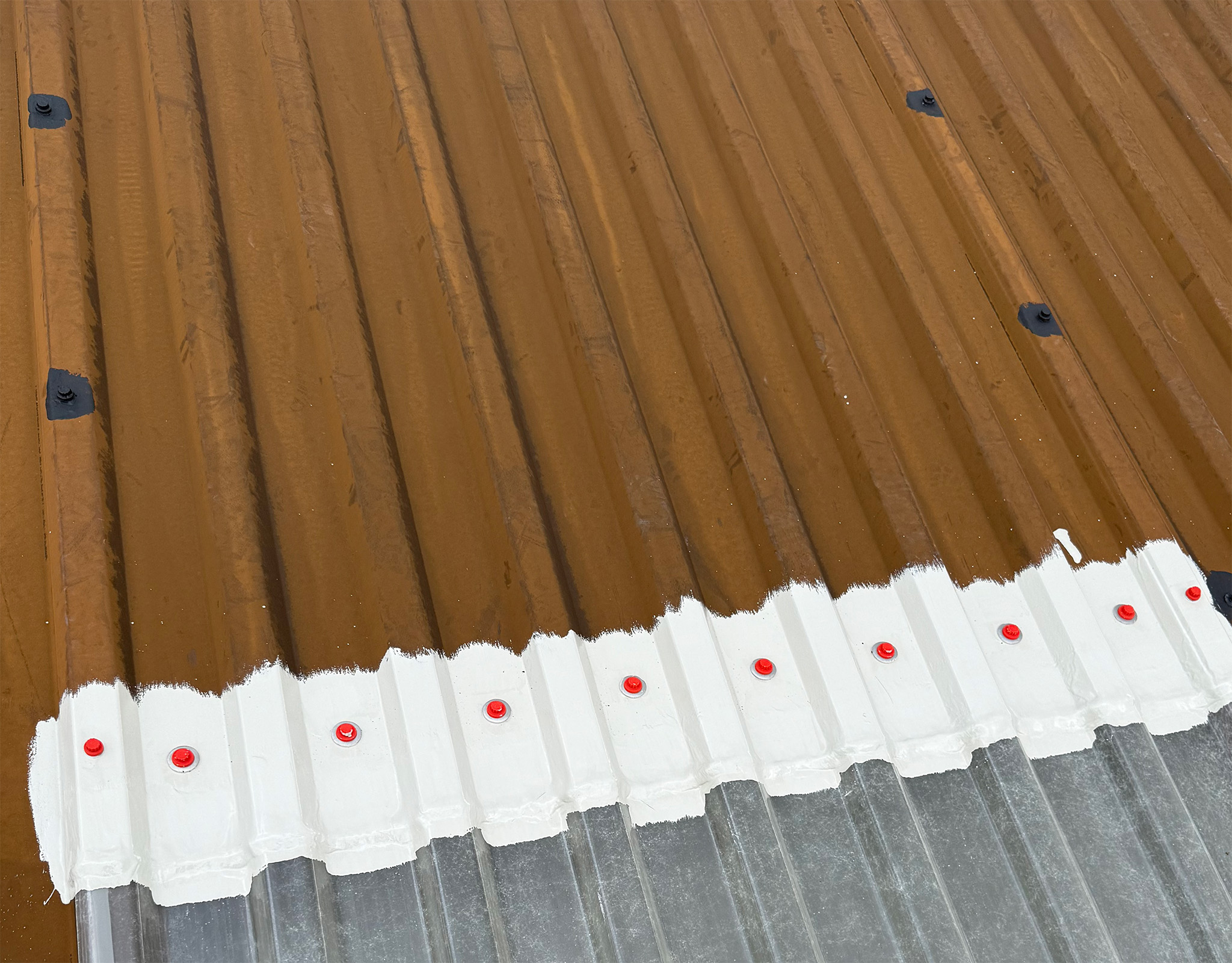 Primed roof fixings and rooflight edges on a corroded steel roof before coating
