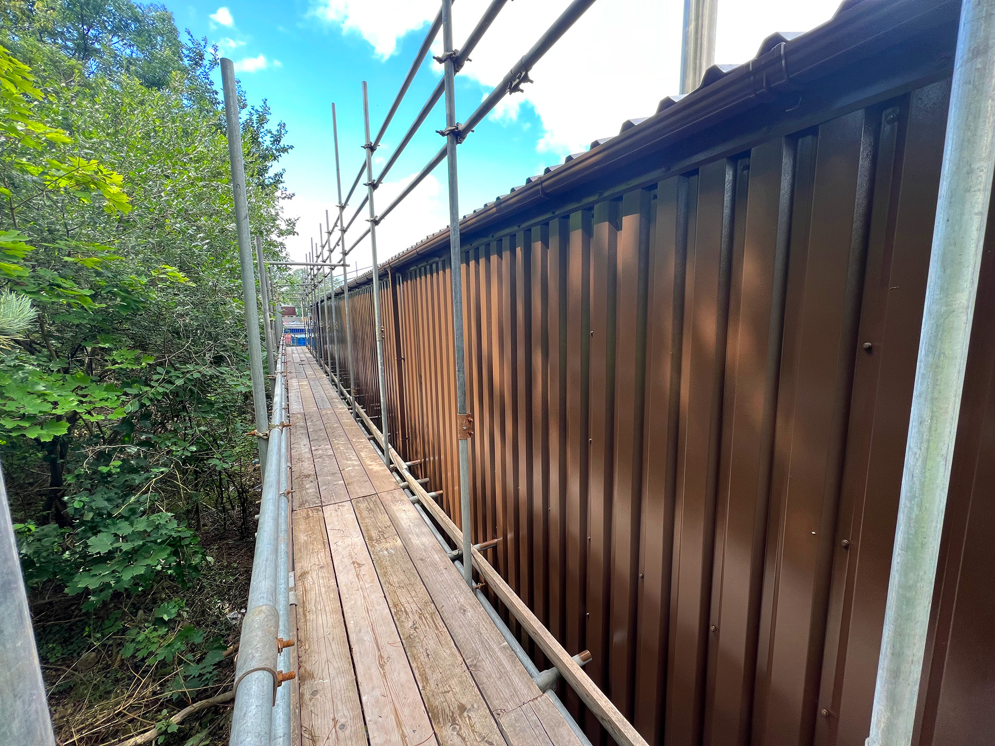 Scaffolding walkway installed along rear elevation for cladding repair and coating access at Bodelwyddan